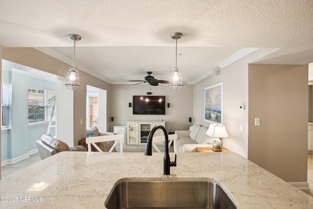 kitchen with pendant lighting, sink, ornamental molding, light stone countertops, and a textured ceiling