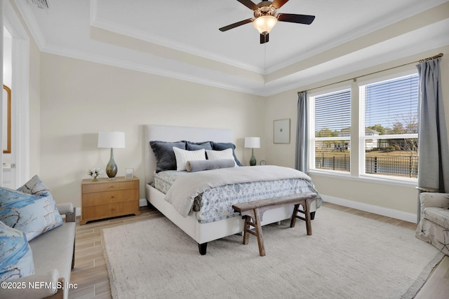 bedroom featuring ceiling fan, ornamental molding, a raised ceiling, and light wood-type flooring