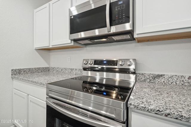 kitchen with light stone counters, appliances with stainless steel finishes, and white cabinets