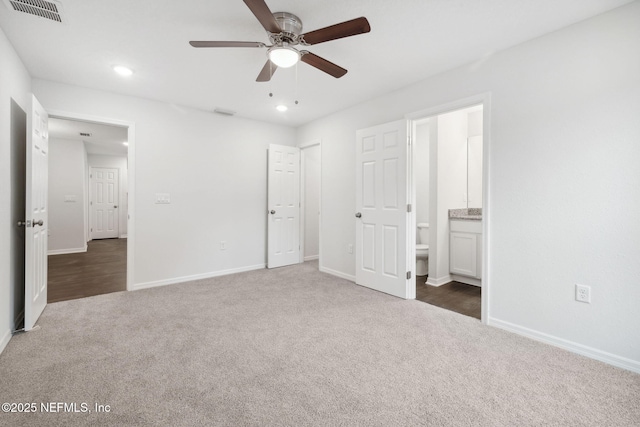 unfurnished bedroom with ceiling fan, ensuite bathroom, and dark carpet