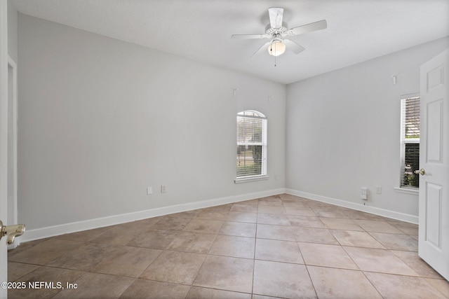 empty room featuring a ceiling fan, light tile patterned flooring, and baseboards