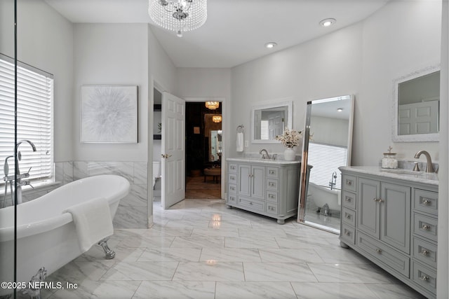 full bath with a freestanding tub, two vanities, a sink, and an inviting chandelier