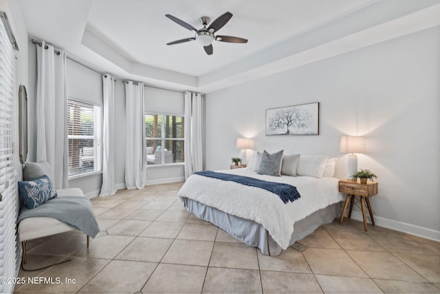 bedroom with light tile patterned flooring, a raised ceiling, a ceiling fan, and baseboards