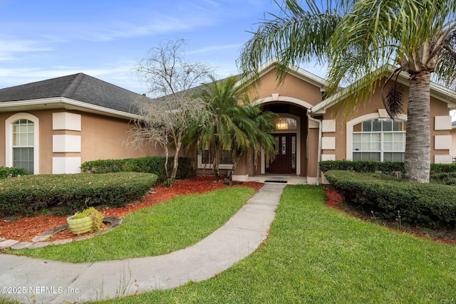 entrance to property featuring roof with shingles, a lawn, and stucco siding