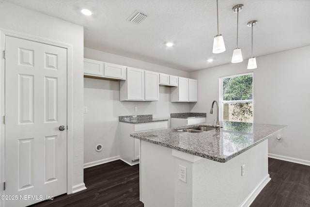 kitchen with sink, a kitchen island with sink, hanging light fixtures, white cabinets, and stone countertops