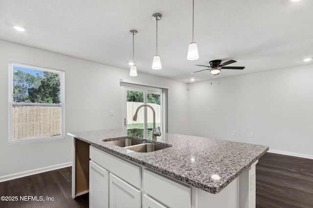 kitchen with sink, dark wood-type flooring, hanging light fixtures, light stone counters, and white cabinets