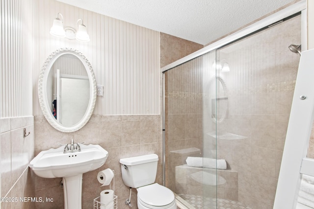 bathroom with sink, tile walls, an enclosed shower, toilet, and a textured ceiling