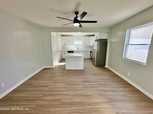 kitchen with a kitchen island, white cabinetry, stainless steel fridge, ceiling fan, and light wood-type flooring