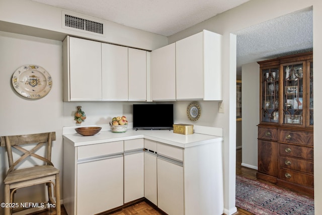 kitchen featuring white cabinetry, parquet flooring, and a textured ceiling