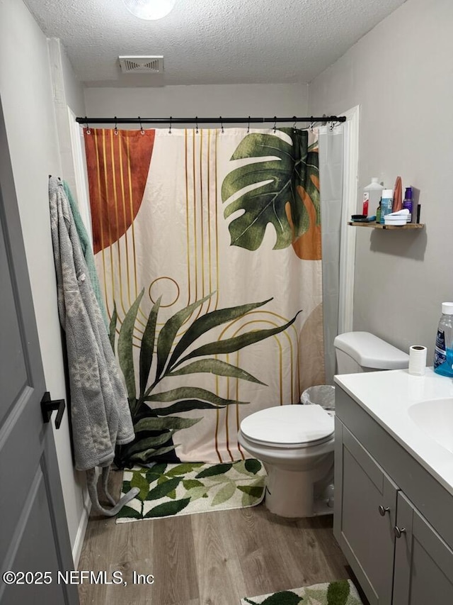 bathroom with wood-type flooring, vanity, walk in shower, toilet, and a textured ceiling