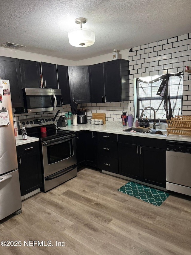 kitchen featuring stainless steel appliances, sink, light hardwood / wood-style flooring, and backsplash