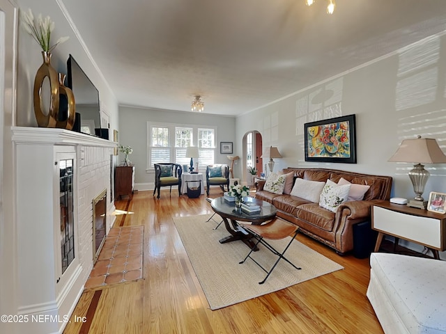 living room with a brick fireplace, crown molding, and light wood-type flooring