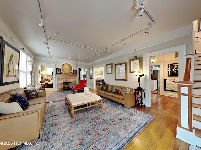 living room featuring crown molding, track lighting, a brick fireplace, and light hardwood / wood-style flooring