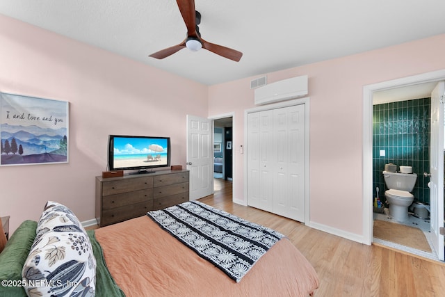 bedroom featuring ensuite bath, light hardwood / wood-style flooring, ceiling fan, a wall unit AC, and a closet