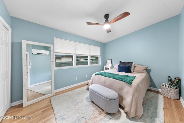 bedroom with hardwood / wood-style flooring, a wall mounted air conditioner, ceiling fan, and a closet