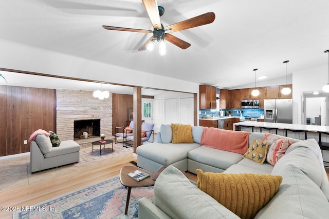 living room featuring lofted ceiling, a stone fireplace, wood walls, light hardwood / wood-style flooring, and ceiling fan