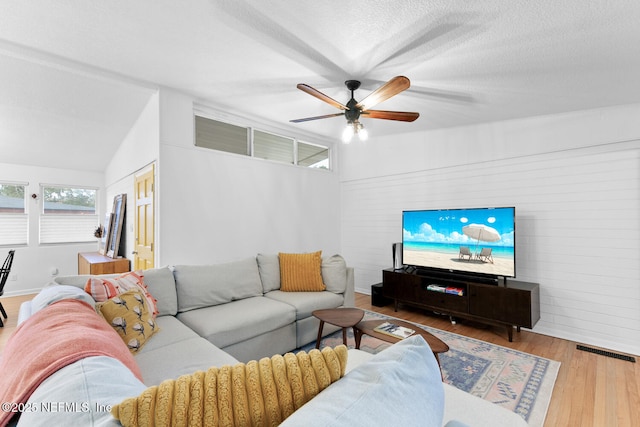 living room with vaulted ceiling, ceiling fan, light hardwood / wood-style floors, and a textured ceiling