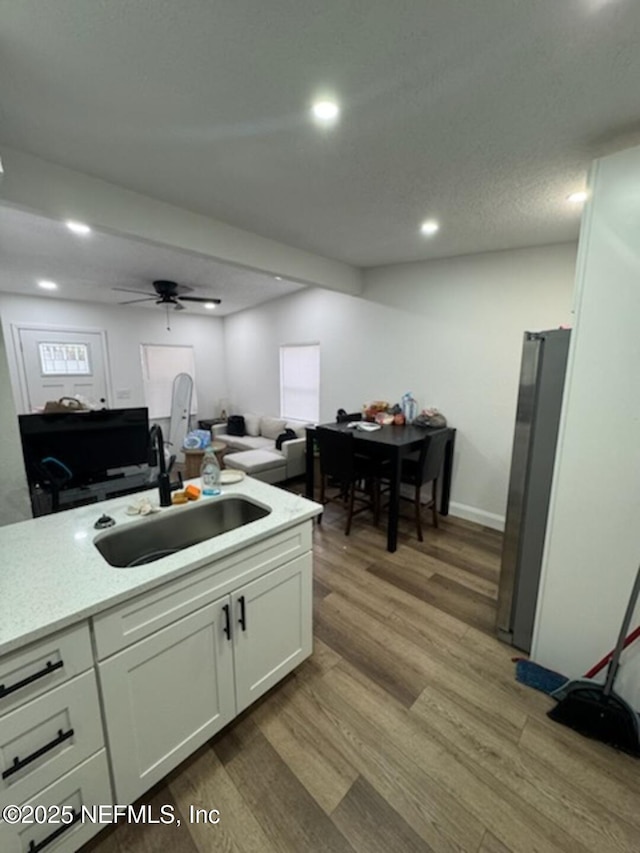 kitchen with stainless steel refrigerator, sink, white cabinets, ceiling fan, and light hardwood / wood-style floors