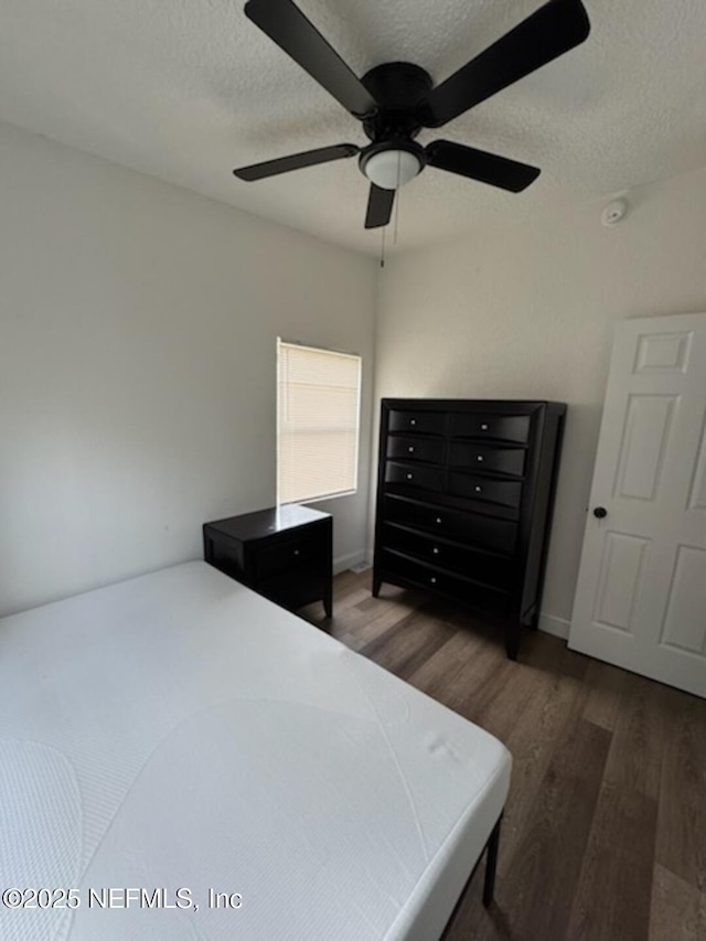 bedroom featuring dark hardwood / wood-style flooring, ceiling fan, and a textured ceiling