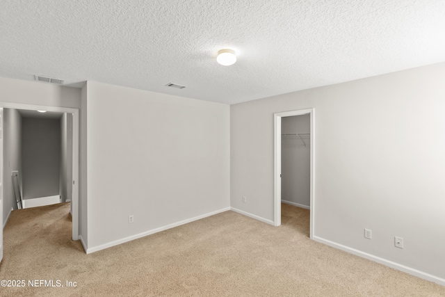 unfurnished bedroom featuring a walk in closet, light colored carpet, a textured ceiling, and a closet