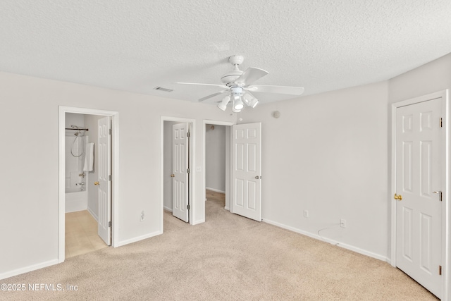 unfurnished bedroom with ceiling fan, connected bathroom, a textured ceiling, light carpet, and a spacious closet