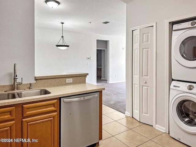 kitchen with light tile patterned flooring, stacked washer / dryer, dishwasher, sink, and hanging light fixtures