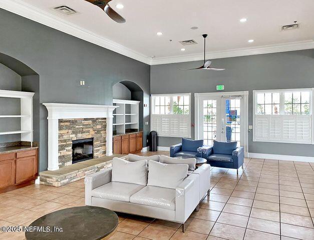 tiled living room featuring crown molding, a stone fireplace, and ceiling fan