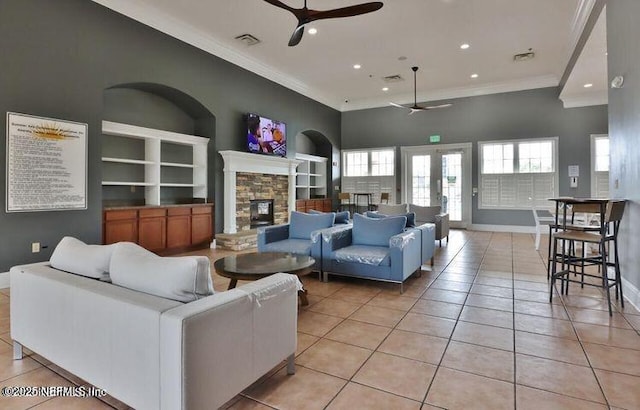 living room featuring light tile patterned flooring, ceiling fan, ornamental molding, and a stone fireplace