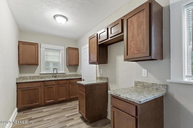 kitchen featuring sink, light hardwood / wood-style flooring, light stone countertops, and a textured ceiling