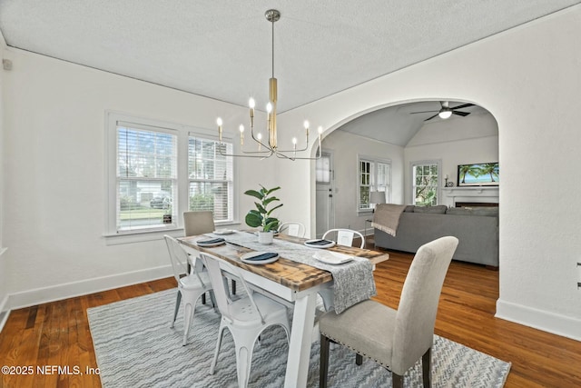 dining room with vaulted ceiling, dark hardwood / wood-style floors, ceiling fan with notable chandelier, and a textured ceiling