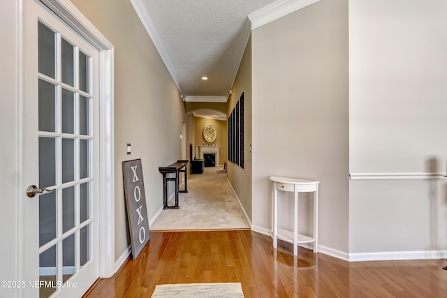 corridor featuring arched walkways, a textured ceiling, wood finished floors, and ornamental molding