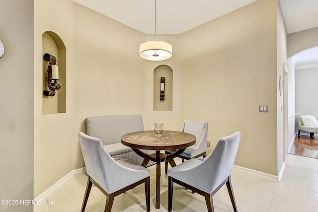 dining area featuring arched walkways, baseboards, and light tile patterned flooring