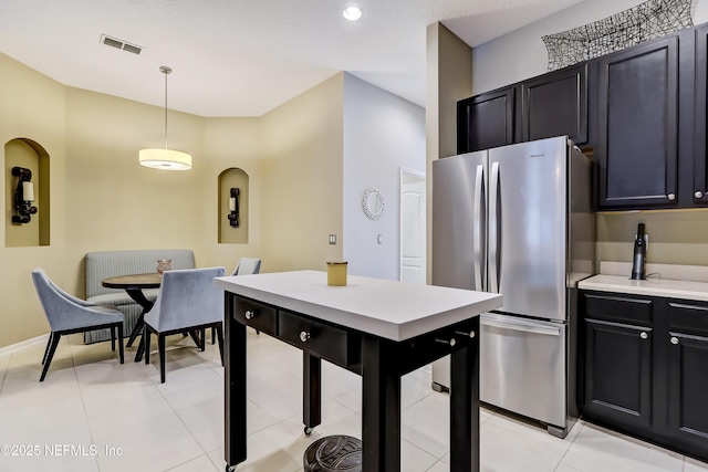 kitchen with visible vents, pendant lighting, light countertops, dark cabinetry, and freestanding refrigerator