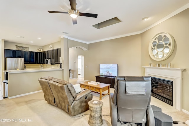 living room with light carpet, a fireplace, crown molding, and a ceiling fan