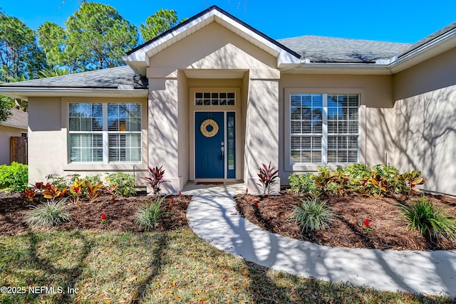 entrance to property featuring a shingled roof and stucco siding