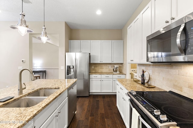 kitchen with sink, stainless steel appliances, light stone counters, white cabinets, and decorative light fixtures