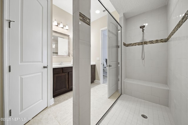 bathroom featuring vanity, tile patterned flooring, a textured ceiling, and a tile shower