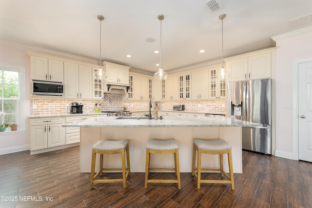 kitchen featuring an island with sink, appliances with stainless steel finishes, ornamental molding, and decorative light fixtures