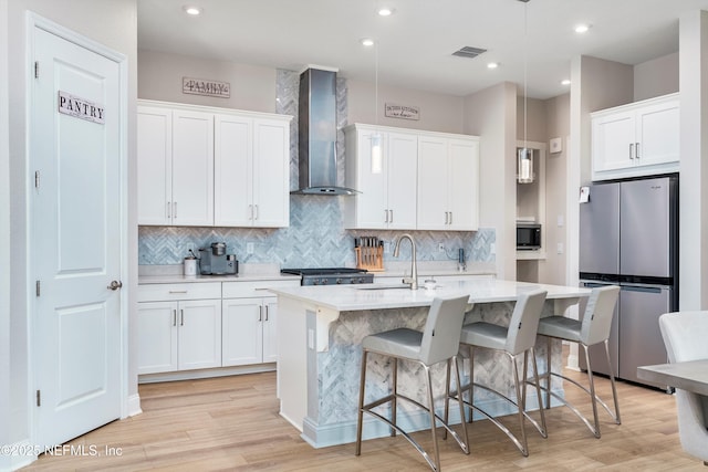 kitchen with stainless steel refrigerator, wall chimney exhaust hood, sink, and white cabinets