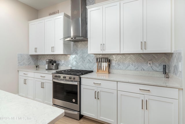 kitchen featuring white cabinetry, stainless steel range with gas stovetop, decorative backsplash, and wall chimney exhaust hood