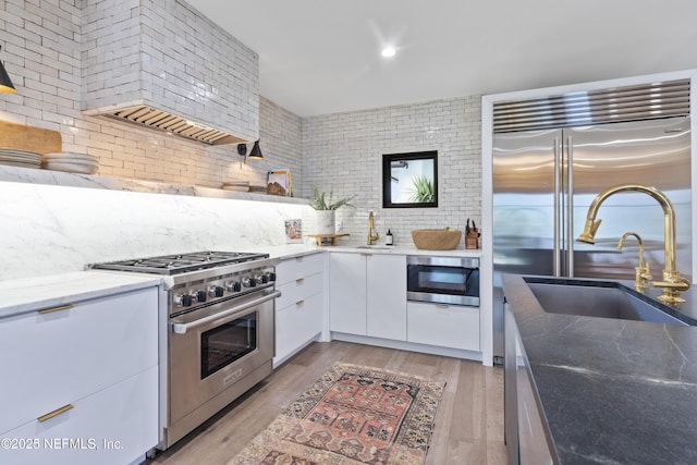 kitchen with light wood finished floors, white cabinets, premium appliances, backsplash, and a sink