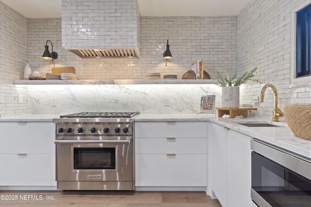 kitchen with light stone countertops, a sink, stainless steel stove, and white cabinetry