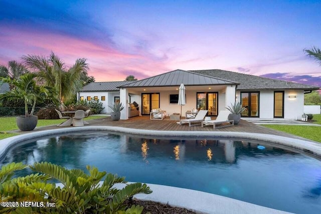 back of property at dusk with an outdoor pool, metal roof, a standing seam roof, a patio area, and stucco siding