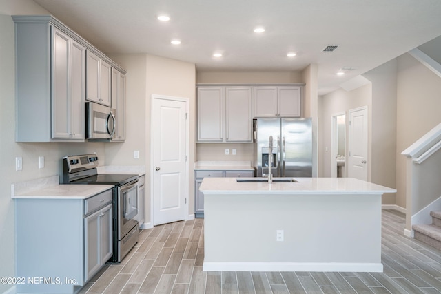 kitchen featuring stainless steel appliances, an island with sink, and gray cabinets