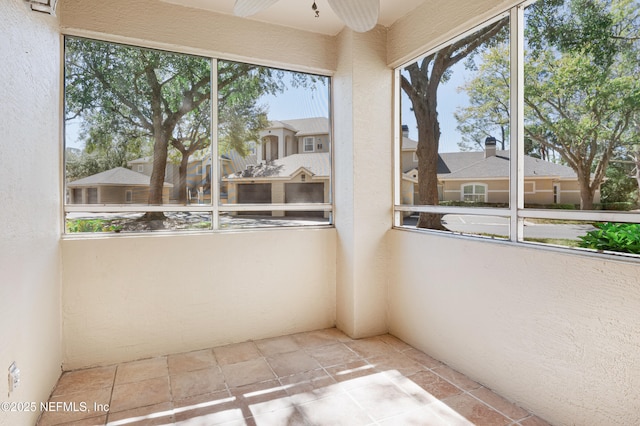 unfurnished sunroom featuring a ceiling fan, a residential view, and plenty of natural light