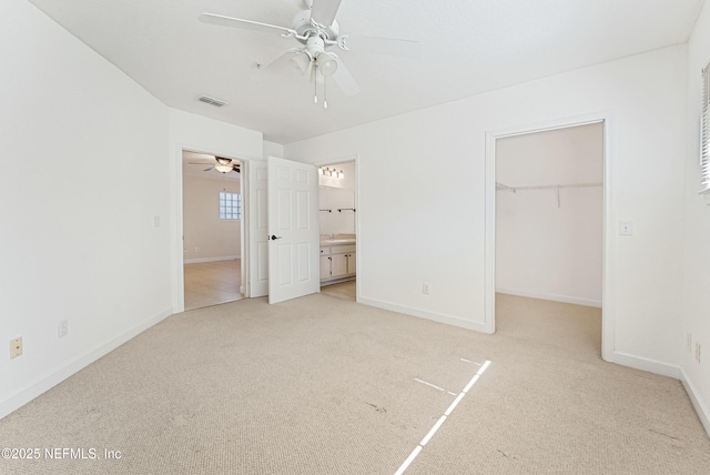 unfurnished bedroom featuring a walk in closet, light colored carpet, visible vents, ensuite bath, and baseboards