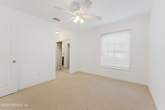 spare room with light colored carpet, ceiling fan, visible vents, and baseboards