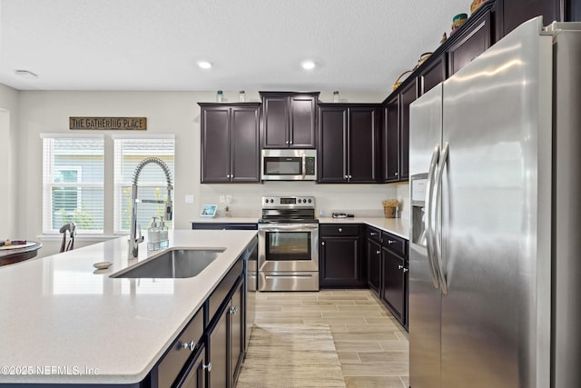 kitchen with sink, stainless steel appliances, light stone countertops, an island with sink, and a textured ceiling