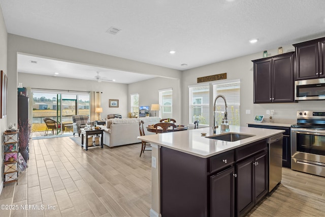 kitchen with sink, ceiling fan, stainless steel appliances, an island with sink, and a textured ceiling