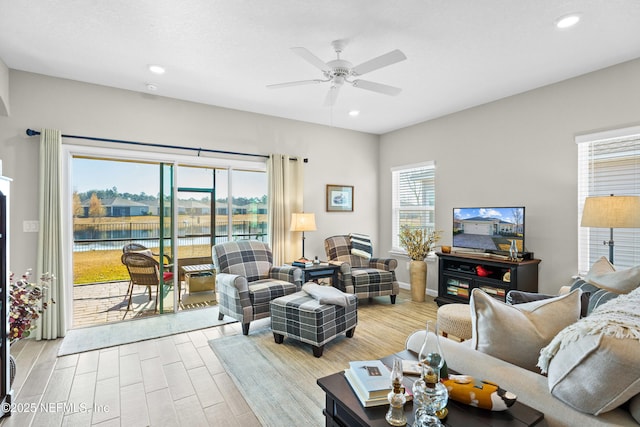 living room featuring light hardwood / wood-style flooring, ceiling fan, and a water view